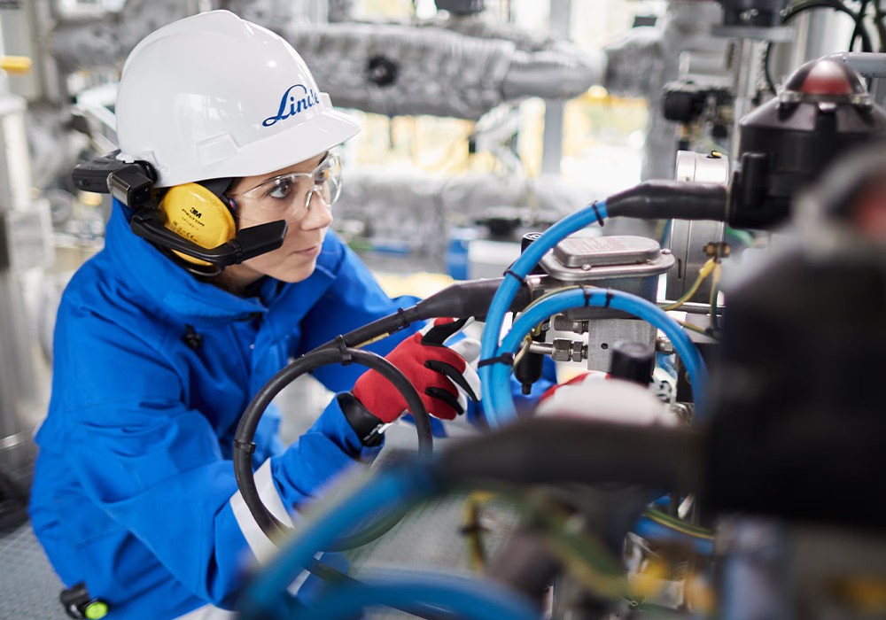 Tecnico in trasferimento con valigia e casco verso un impianto industriale remoto: simbolo delle criticità operative e ambientali della manutenzione tradizionale